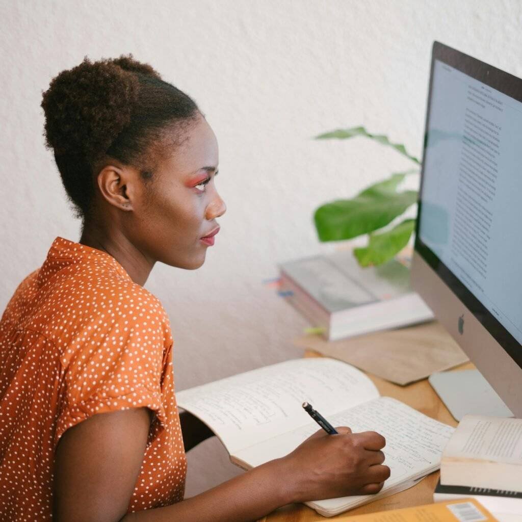 A focused young woman studying with books and a computer at her home office desk.