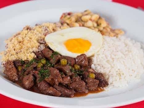 A plate of Brazilian feijoada with rice, beans, farofa, and a fried egg.