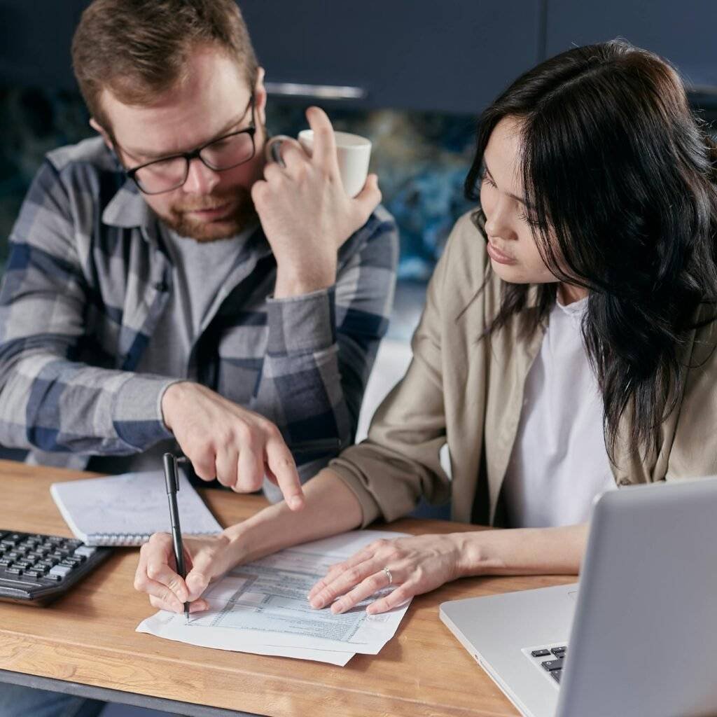 A couple analyzing financial documents with calculator and laptop on a table.