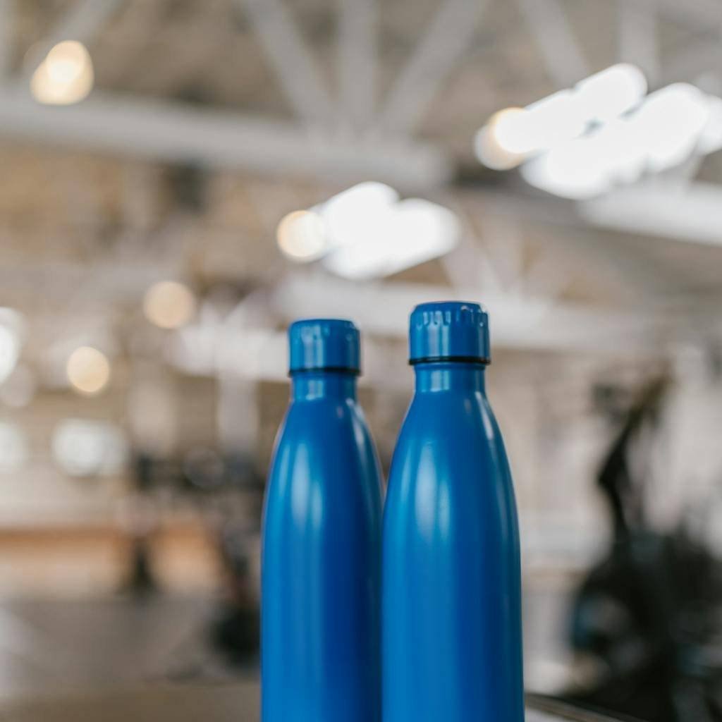 Close-up of two blue water bottles against a blurred indoor background.