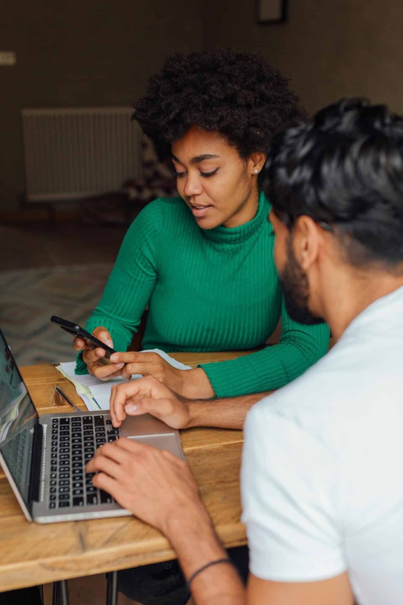 Two adults collaborating on a project at home with a laptop and smartphone.