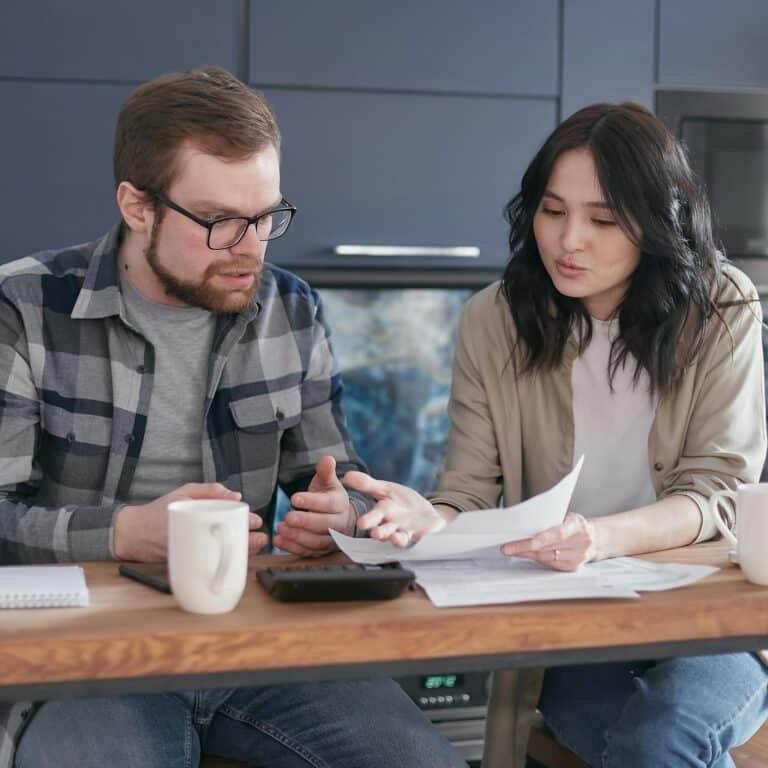 A couple having a serious discussion and reviewing documents at a kitchen table.